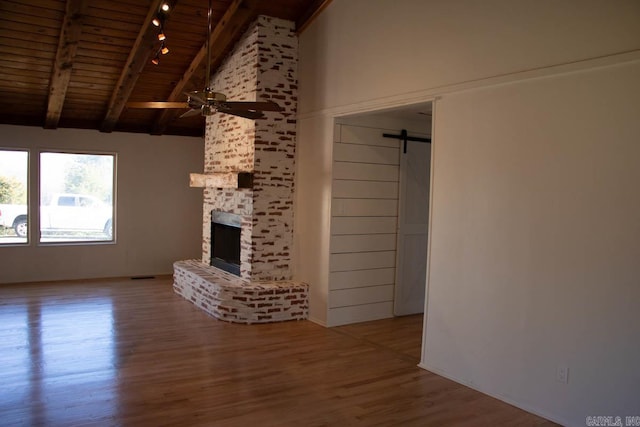 unfurnished living room with ceiling fan, a brick fireplace, a barn door, wooden ceiling, and hardwood / wood-style floors