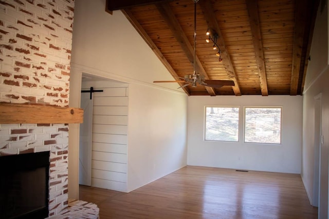 unfurnished living room with a fireplace, wooden ceiling, a barn door, and vaulted ceiling with beams