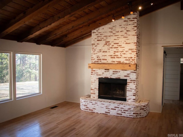 unfurnished living room with a large fireplace, a healthy amount of sunlight, hardwood / wood-style floors, and vaulted ceiling with beams