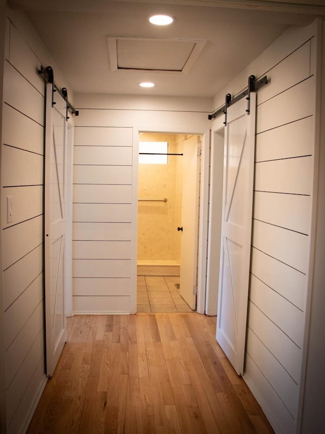 hall with wood walls, a barn door, and light hardwood / wood-style floors