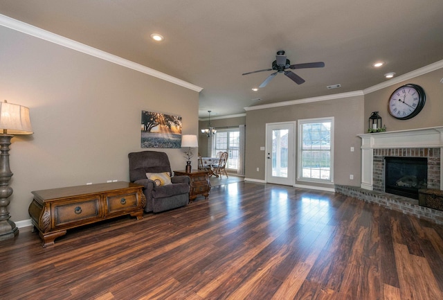 living room with ceiling fan with notable chandelier, dark wood-type flooring, crown molding, and a fireplace