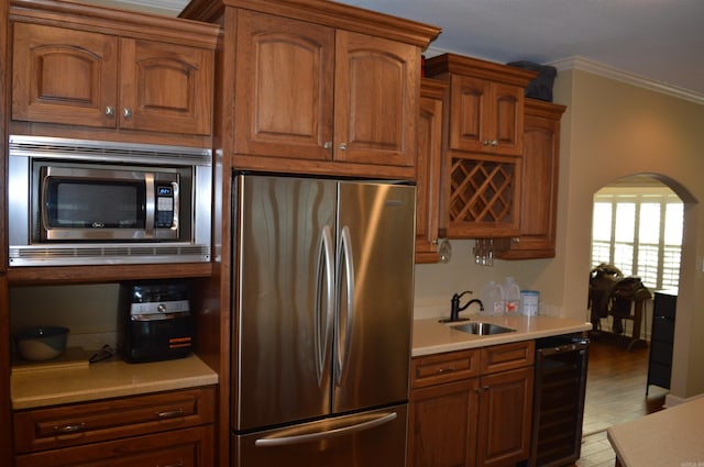 kitchen with crown molding, light hardwood / wood-style floors, appliances with stainless steel finishes, sink, and beverage cooler