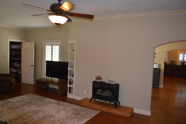 living room with crown molding, dark wood-type flooring, ceiling fan, and a wood stove