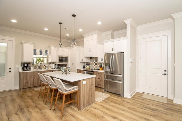 kitchen with a kitchen island, white cabinetry, hanging light fixtures, and appliances with stainless steel finishes