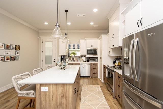 kitchen featuring hanging light fixtures, appliances with stainless steel finishes, white cabinets, a center island, and a breakfast bar area