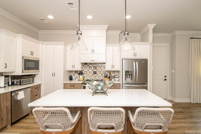 kitchen with white cabinets, stainless steel appliances, a kitchen island, and pendant lighting