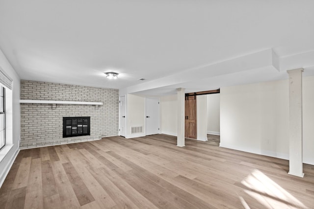 unfurnished living room with decorative columns, light hardwood / wood-style floors, and a brick fireplace