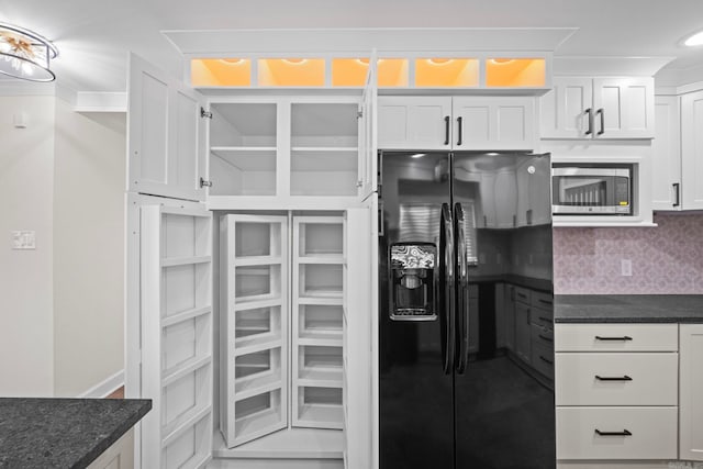 kitchen with stainless steel microwave, black fridge with ice dispenser, backsplash, white cabinetry, and dark stone counters