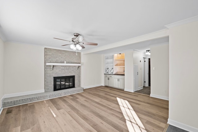 unfurnished living room featuring light wood-type flooring, ceiling fan, a brick fireplace, and ornamental molding