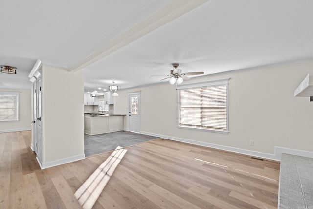 unfurnished living room featuring plenty of natural light, ceiling fan with notable chandelier, and light hardwood / wood-style floors