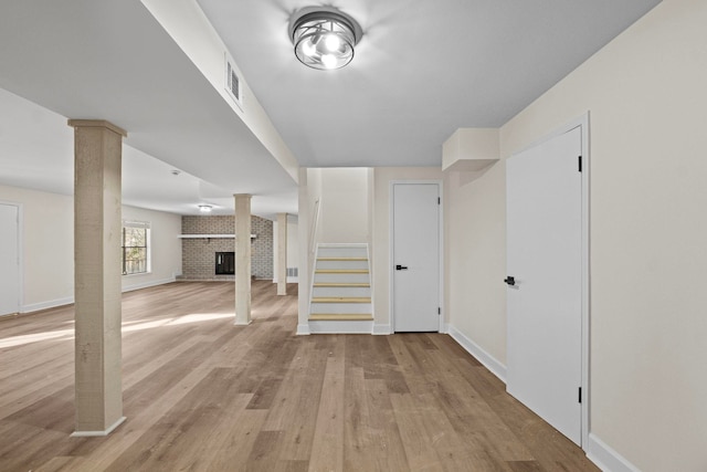 interior space with decorative columns, a brick fireplace, and light hardwood / wood-style flooring