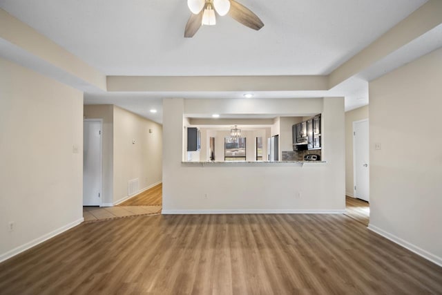 unfurnished living room with ceiling fan with notable chandelier and wood-type flooring