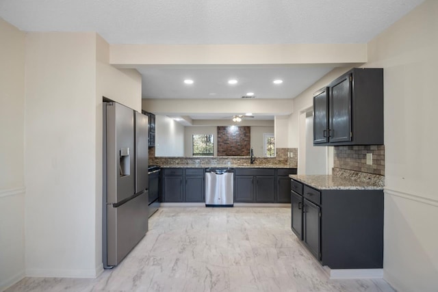 kitchen featuring appliances with stainless steel finishes, sink, tasteful backsplash, light stone counters, and a textured ceiling