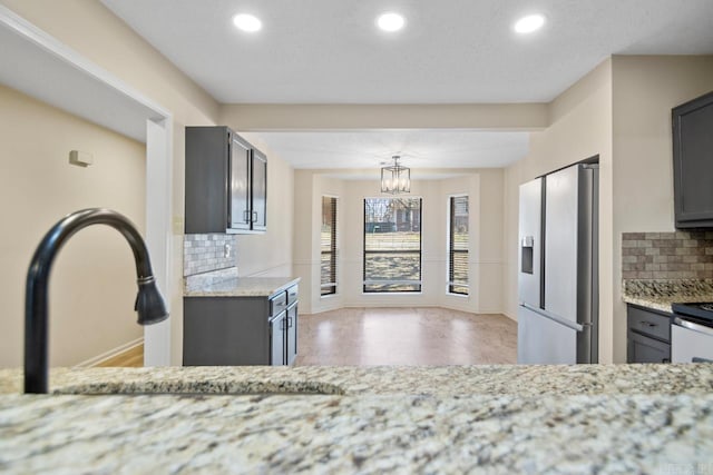 kitchen featuring stainless steel refrigerator with ice dispenser, hanging light fixtures, backsplash, light stone counters, and an inviting chandelier