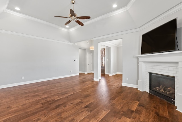 unfurnished living room with crown molding, a brick fireplace, dark wood-type flooring, and ceiling fan