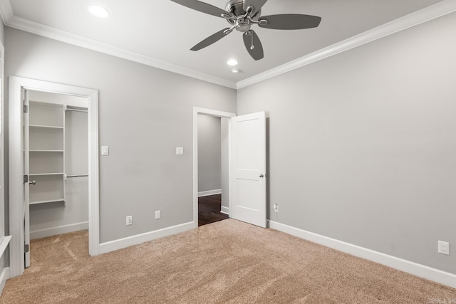 unfurnished bedroom featuring crown molding, carpet floors, ceiling fan, and a spacious closet