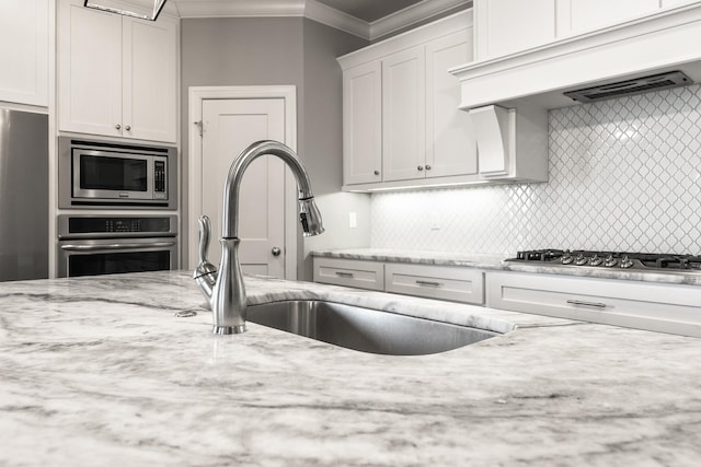 kitchen featuring appliances with stainless steel finishes, white cabinetry, light stone counters, ornamental molding, and custom exhaust hood