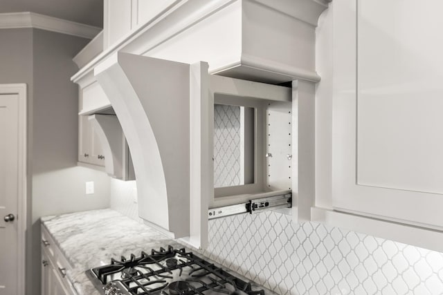 interior space featuring white cabinetry, gas stovetop, light stone counters, and ornamental molding