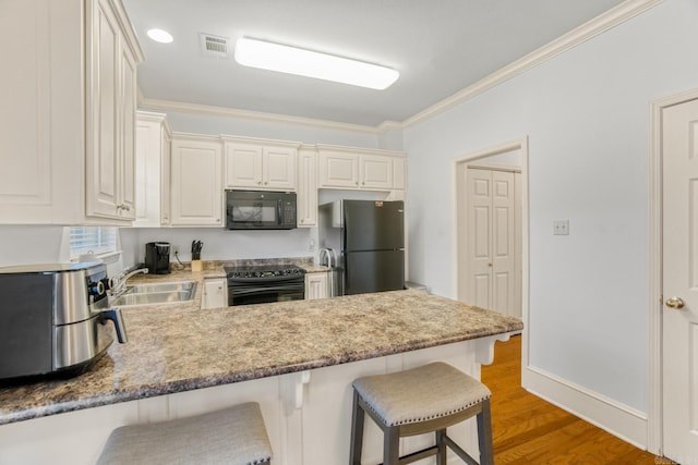 kitchen featuring black appliances, sink, ornamental molding, a breakfast bar, and dark hardwood / wood-style floors