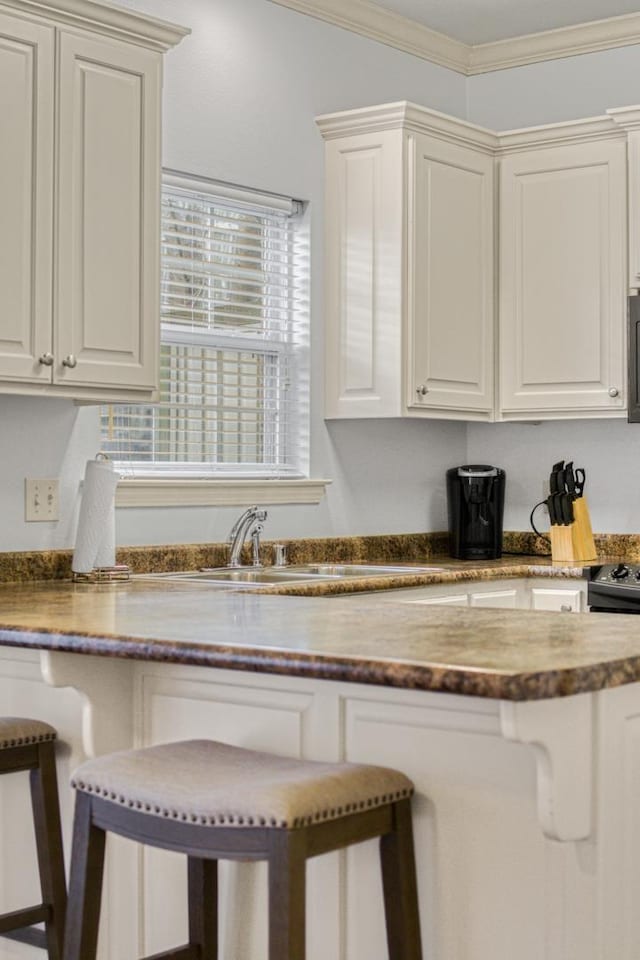 kitchen featuring a breakfast bar, white cabinetry, sink, and crown molding