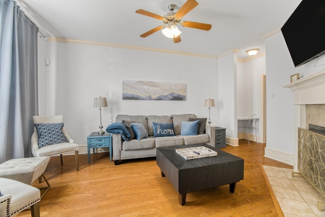 living room with a fireplace, crown molding, ceiling fan, and light wood-type flooring