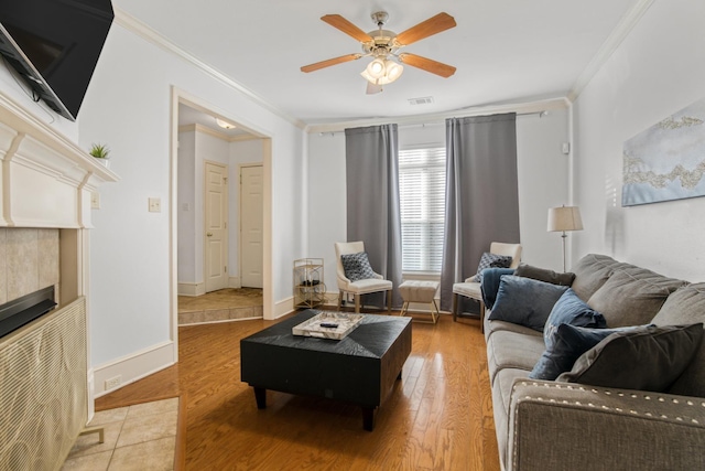 living room with hardwood / wood-style flooring, ceiling fan, crown molding, and a tiled fireplace