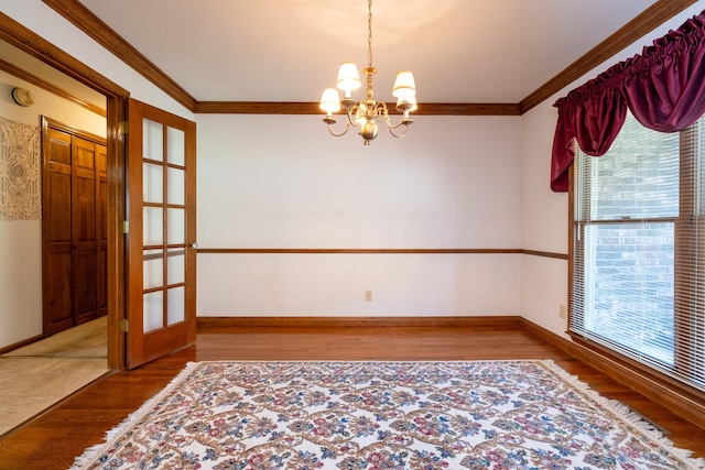 spare room featuring french doors, wood-type flooring, ornamental molding, and a chandelier