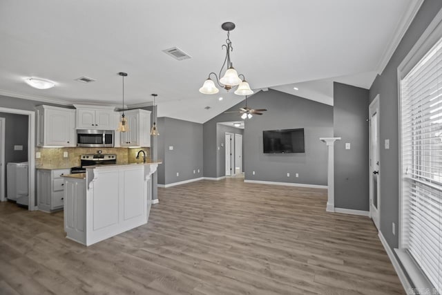 kitchen featuring vaulted ceiling, tasteful backsplash, white cabinetry, decorative light fixtures, and stainless steel appliances