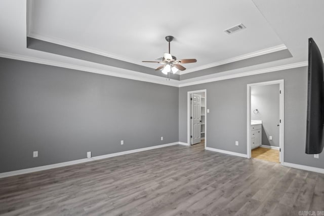 unfurnished bedroom with crown molding, ensuite bath, light wood-type flooring, a raised ceiling, and ceiling fan