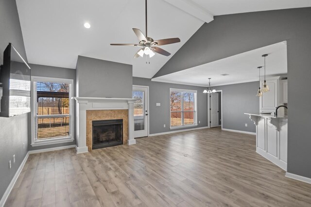 unfurnished living room featuring a tiled fireplace, light hardwood / wood-style floors, ceiling fan with notable chandelier, and beam ceiling