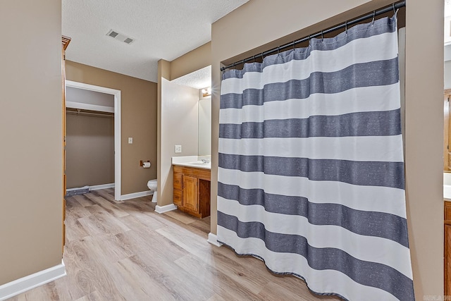 bathroom featuring toilet, a textured ceiling, wood-type flooring, walk in shower, and vanity