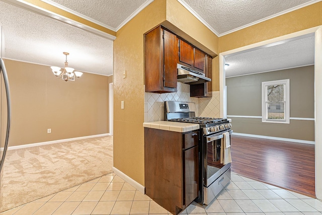 kitchen with pendant lighting, stainless steel gas stove, tile countertops, light tile patterned flooring, and crown molding