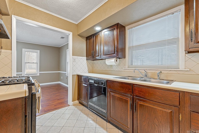 kitchen with black dishwasher, crown molding, sink, stainless steel gas range oven, and light tile patterned flooring