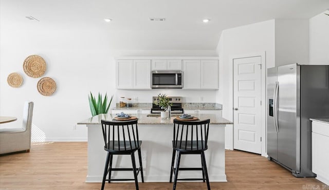 kitchen featuring light stone counters, white cabinets, a kitchen island with sink, and stainless steel appliances