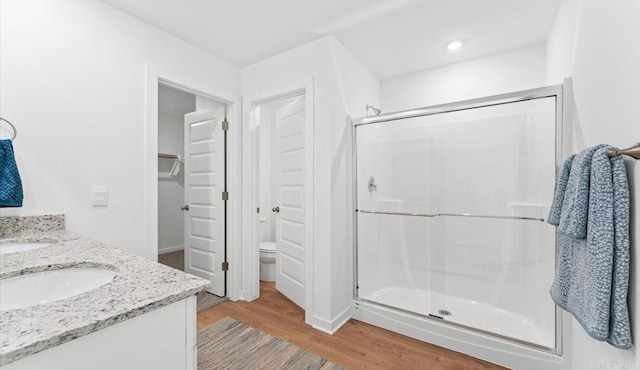 bathroom featuring hardwood / wood-style floors, a shower with door, toilet, and vanity