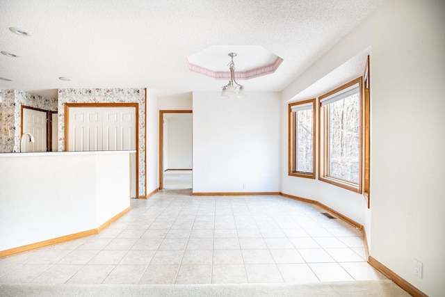 unfurnished room with light tile patterned floors, a textured ceiling, and a tray ceiling