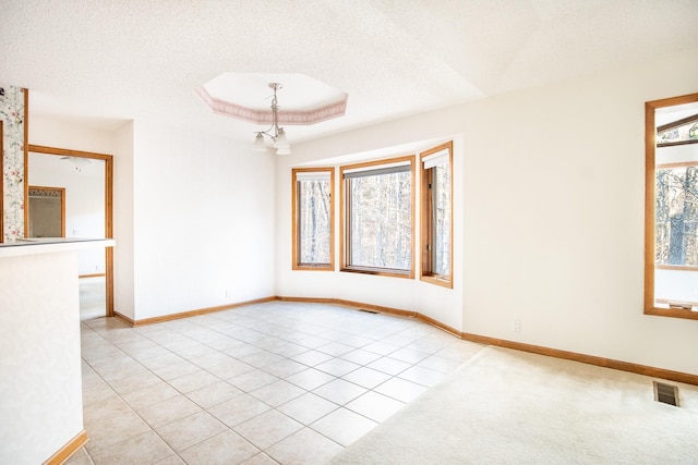 tiled spare room featuring a raised ceiling, an inviting chandelier, and a textured ceiling