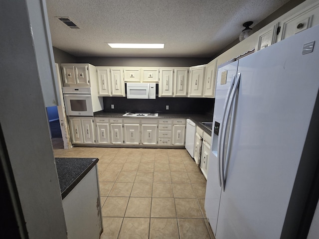 kitchen with white cabinetry, white appliances, a textured ceiling, and light tile patterned flooring