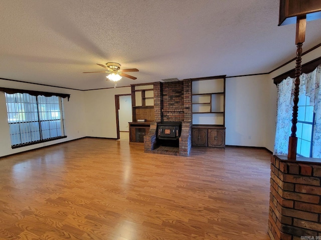 unfurnished living room featuring ceiling fan, light wood-type flooring, a wood stove, a textured ceiling, and ornamental molding