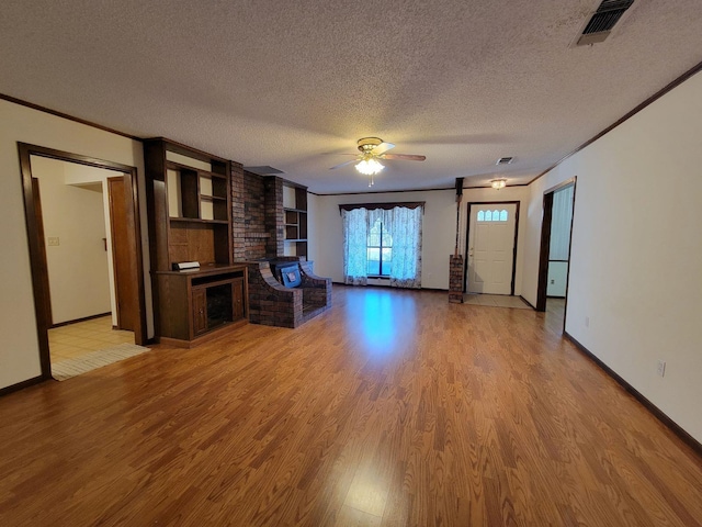 unfurnished living room with a textured ceiling, a fireplace, light wood-type flooring, ceiling fan, and crown molding