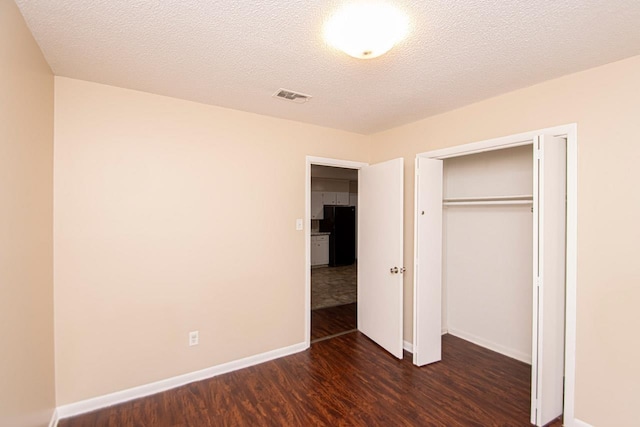 unfurnished bedroom featuring dark wood-type flooring, a textured ceiling, a closet, and black fridge