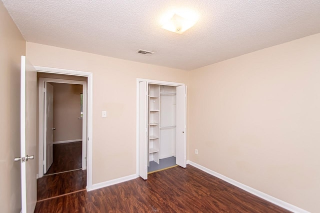 unfurnished bedroom with a textured ceiling, dark hardwood / wood-style floors, and a closet