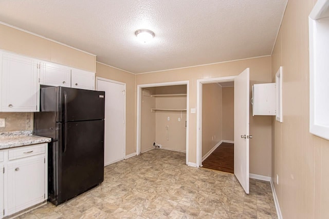 kitchen with black refrigerator, a textured ceiling, and white cabinets