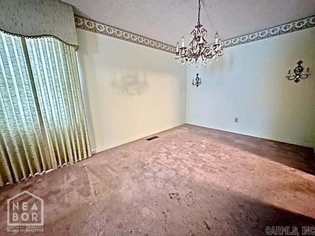 unfurnished dining area featuring carpet floors, a textured ceiling, and an inviting chandelier