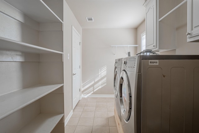 clothes washing area featuring washer and dryer, cabinets, and light tile patterned flooring