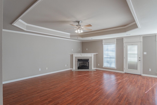 unfurnished living room with crown molding, hardwood / wood-style floors, a tile fireplace, ceiling fan, and a tray ceiling