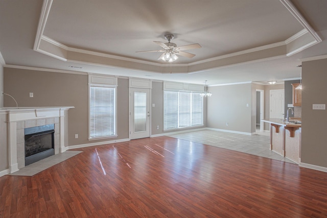 unfurnished living room with a tray ceiling, a tile fireplace, and crown molding