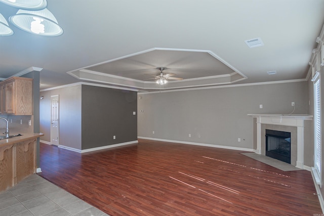 unfurnished living room featuring light hardwood / wood-style floors, a tile fireplace, sink, ornamental molding, and ceiling fan