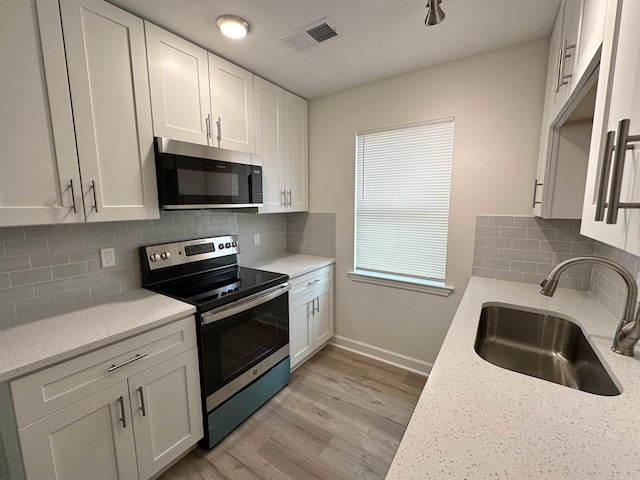 kitchen with appliances with stainless steel finishes, sink, tasteful backsplash, white cabinetry, and light stone countertops