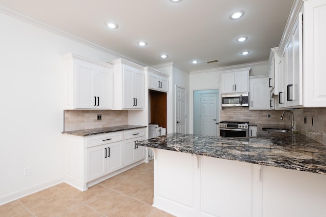 kitchen with kitchen peninsula, appliances with stainless steel finishes, sink, white cabinetry, and dark stone countertops